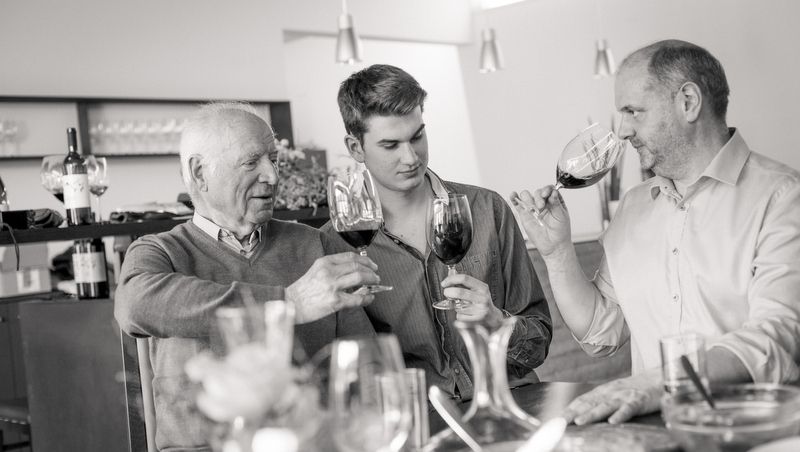 Three men clink glasses of wine at a table.
