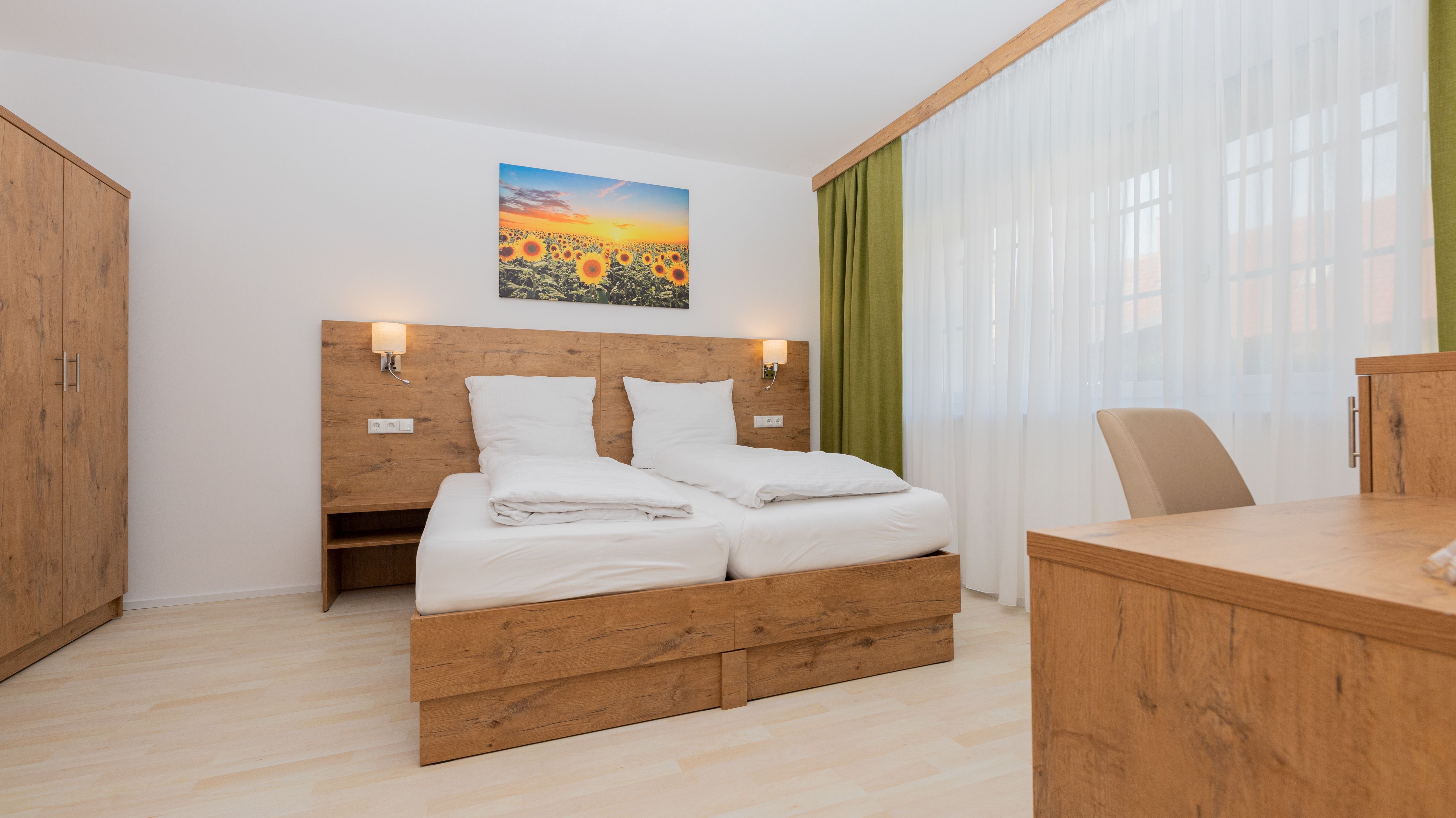 Modern bedroom with wooden furniture, double bed, wardrobe and desk. A picture of sunflowers hangs above the bed.