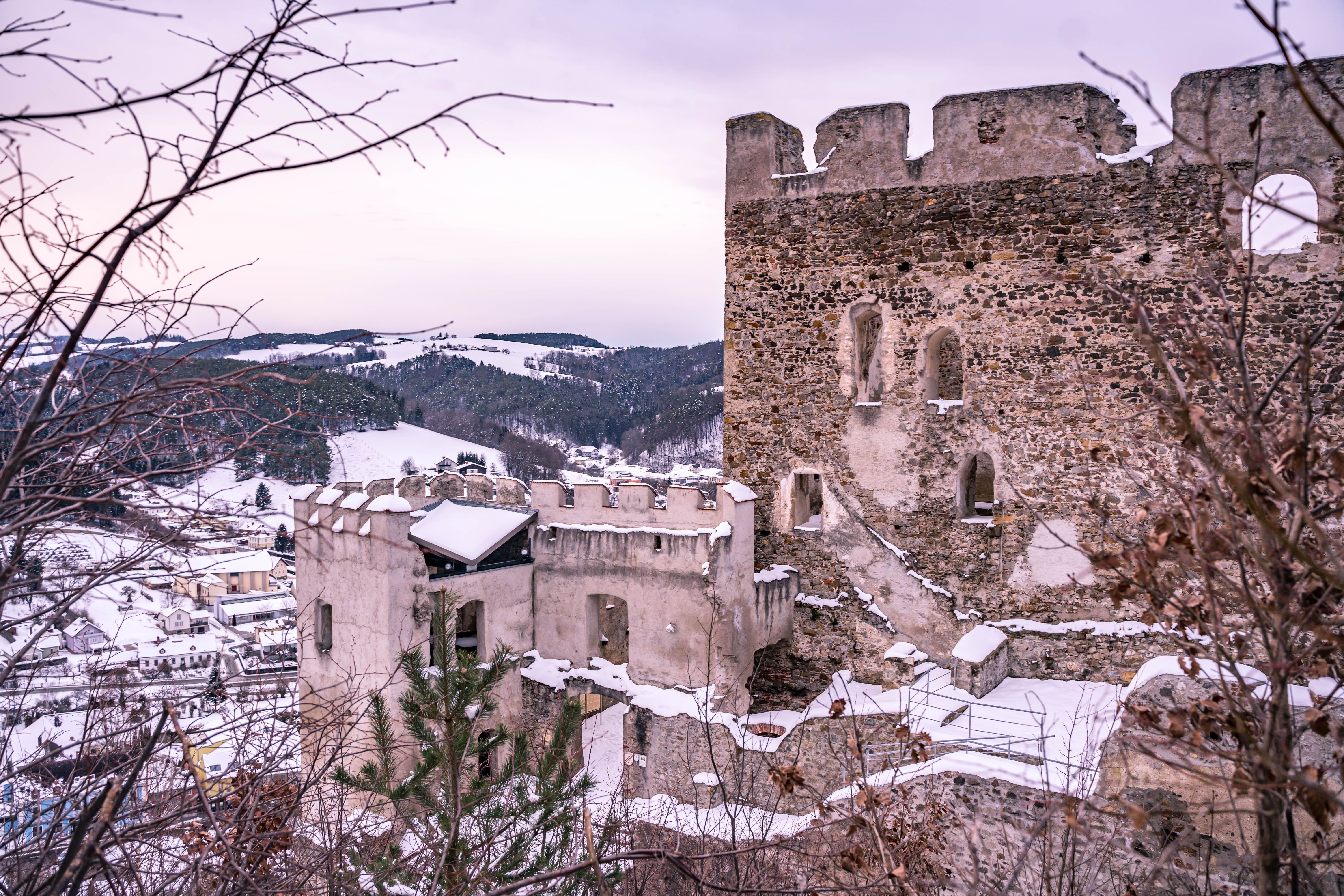 Winter ruins of Kirchschlag Castle in Austria with snow-covered walls and hills in the background.