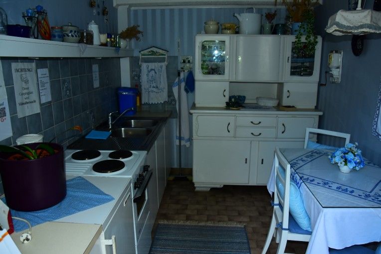 Small, cozy kitchen with blue and white decoration, a stove, sink, cupboard and small dining table.