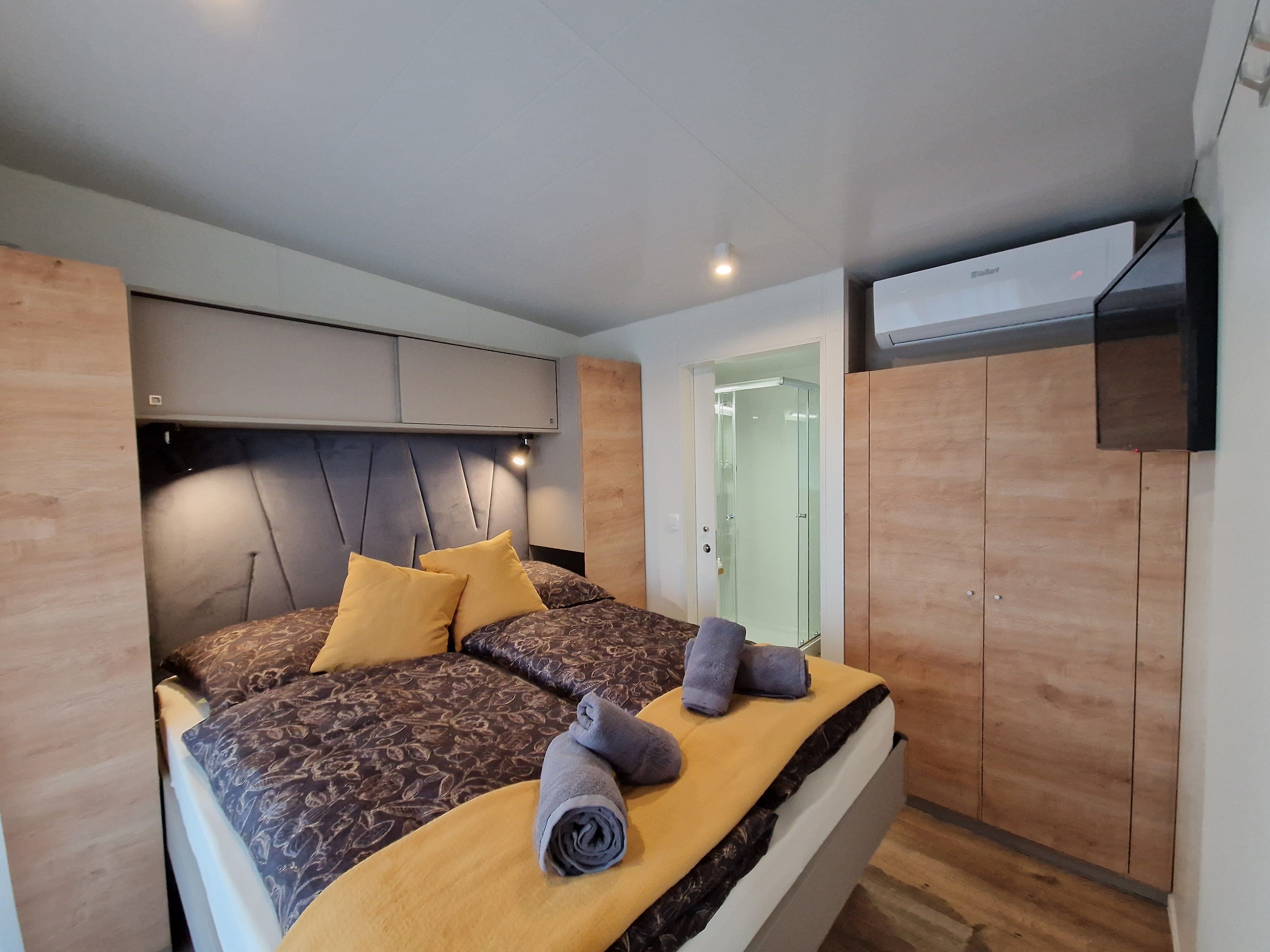Interior view of a bedroom with double bed, yellow pillows and towels, wardrobe, air conditioning and view of the bathroom.