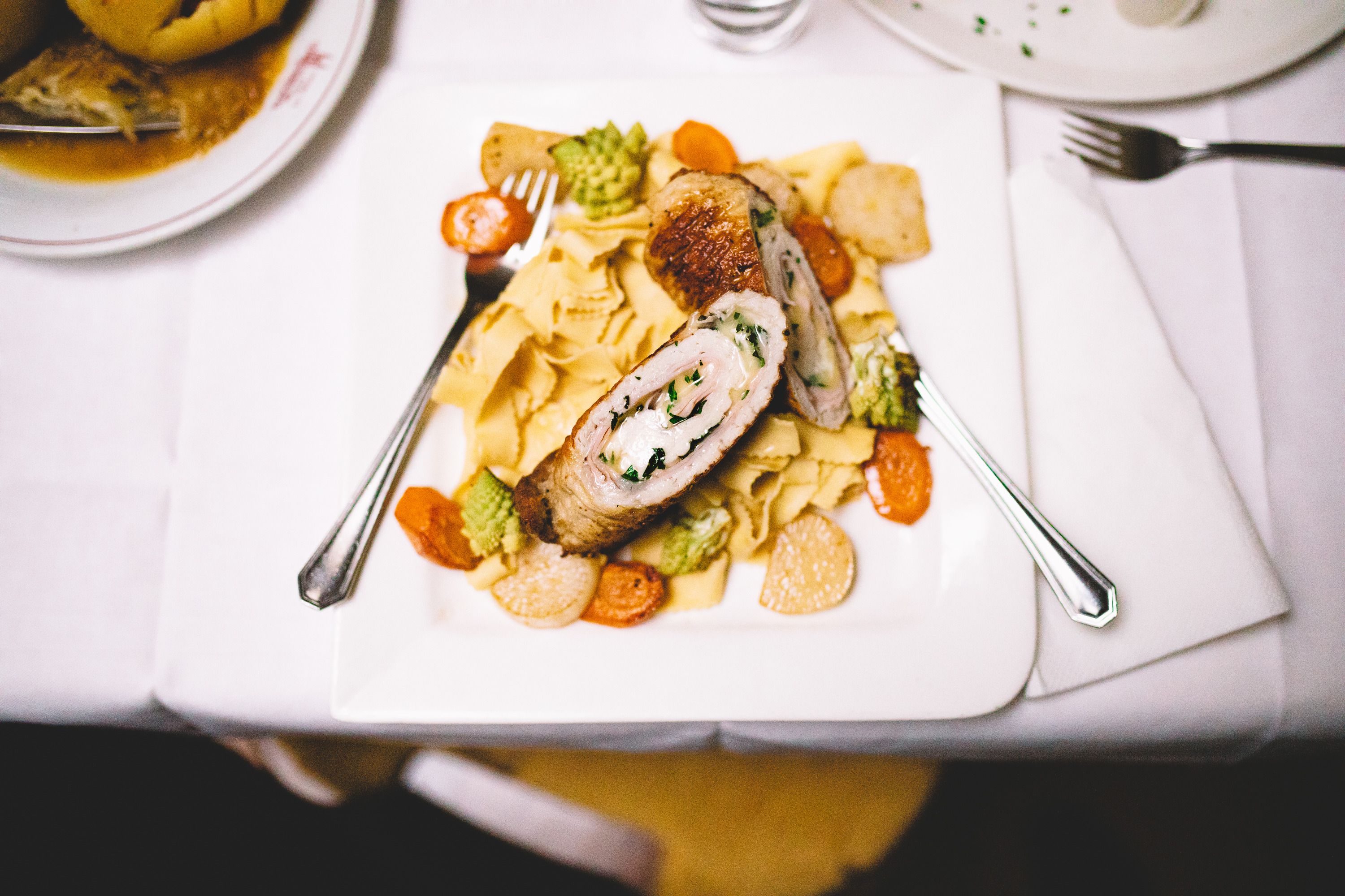 Stuffed meat on noodles with vegetables on a white plate.