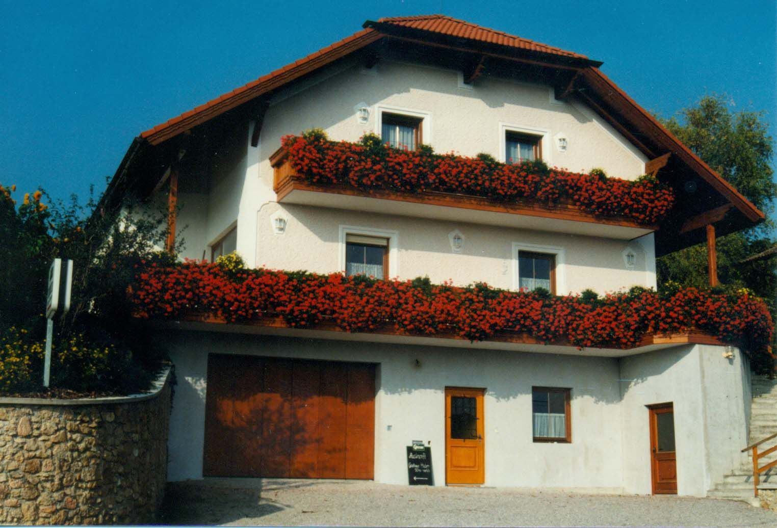 A traditional guest house with red flowers on the balconies and a red roof.