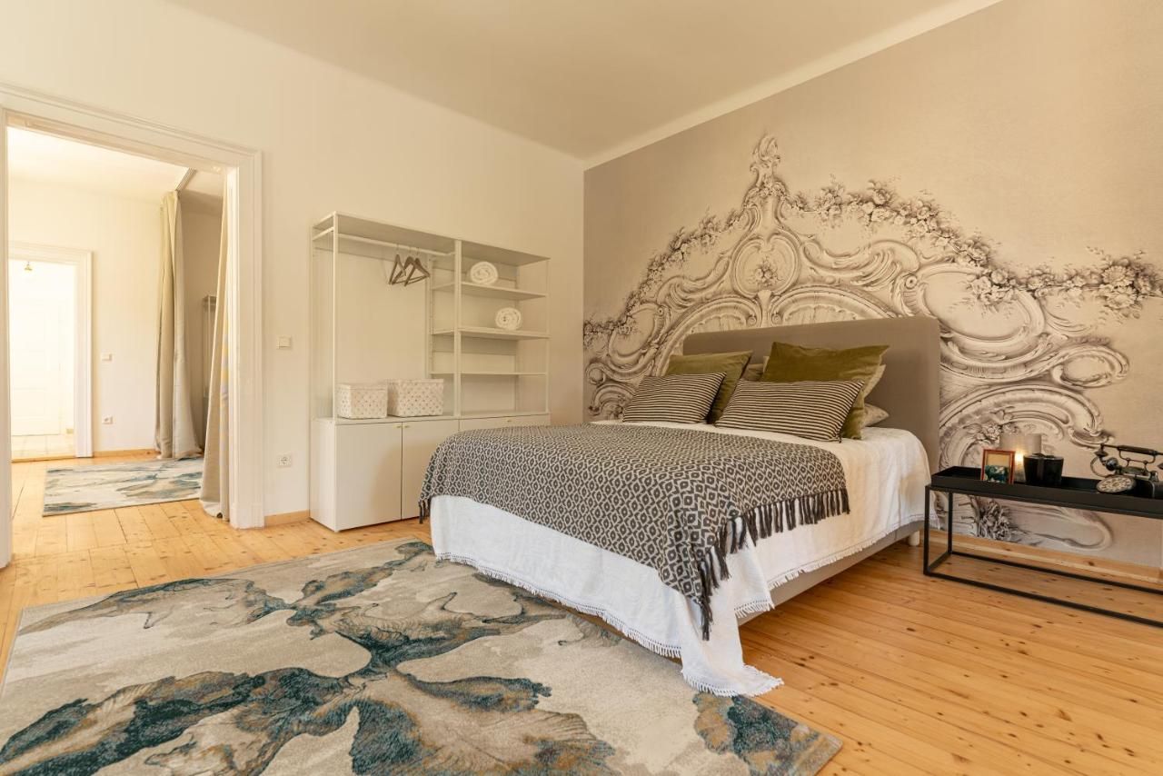 A stylishly furnished bedroom with a large bed, decorative cushions, a rug and an artistic wall design.