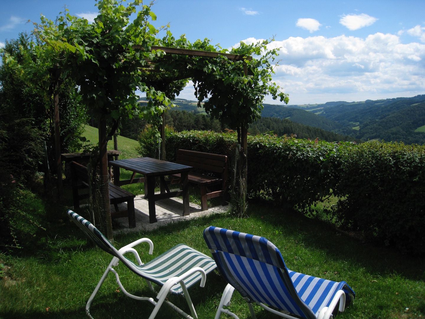 Gazebo with table and benches, surrounded by green landscape and two deckchairs in the foreground.