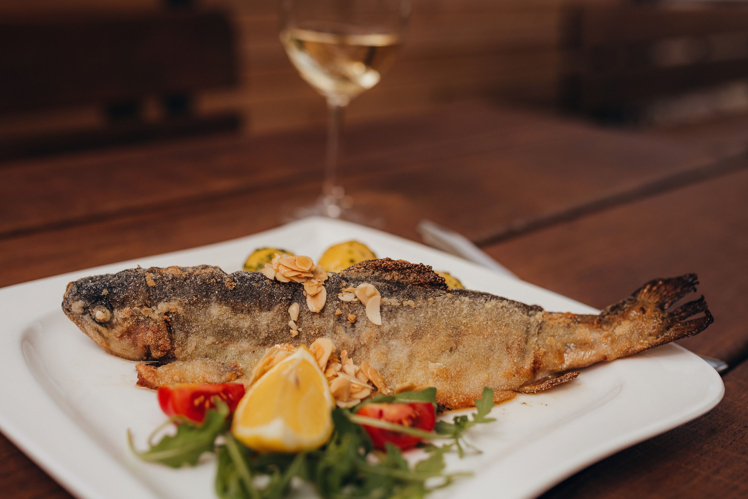 Fried trout with almond butter on a plate, garnished with lemon and vegetables.