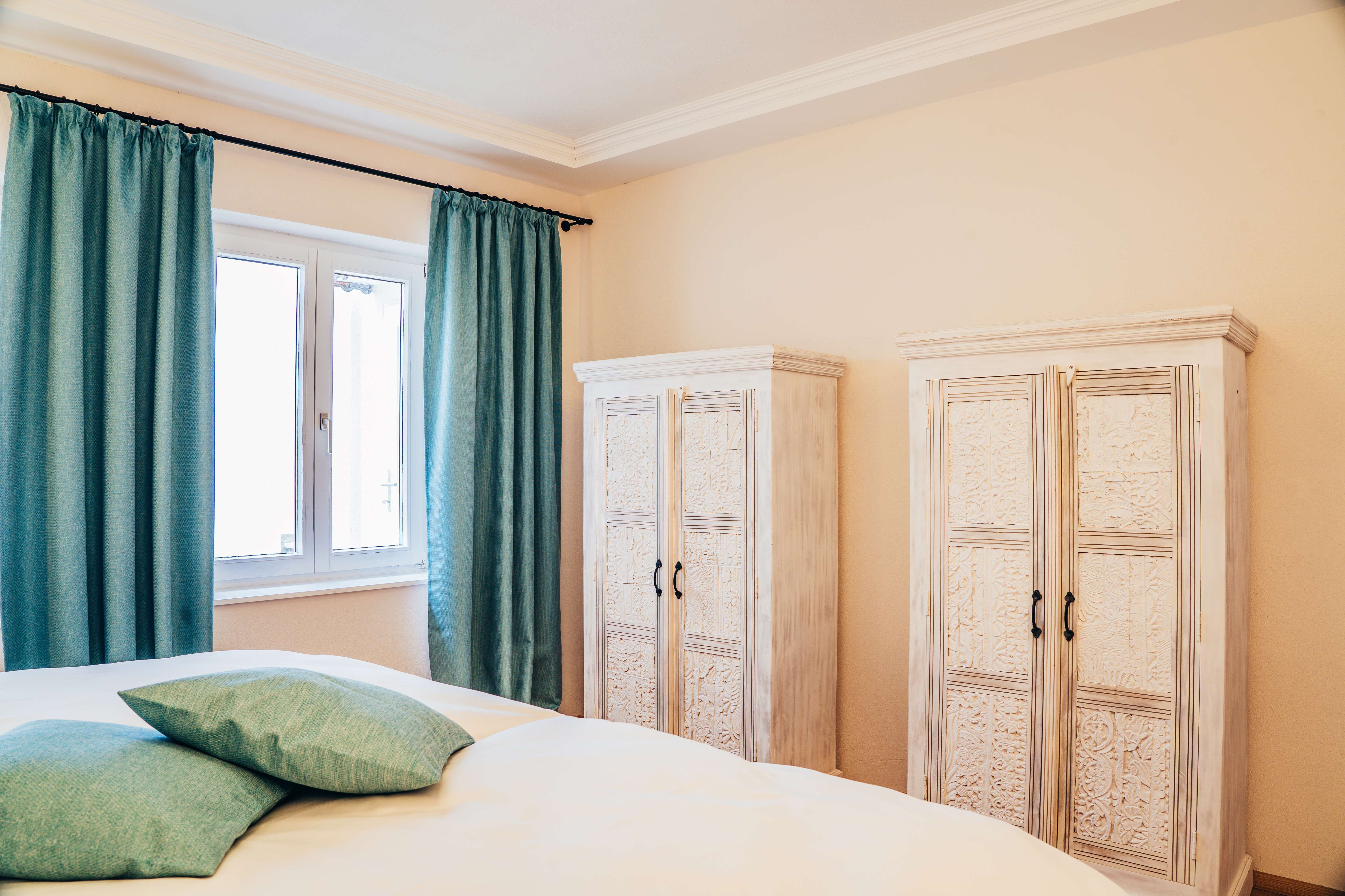Bedroom with two white wardrobes, turquoise curtains and cushions.