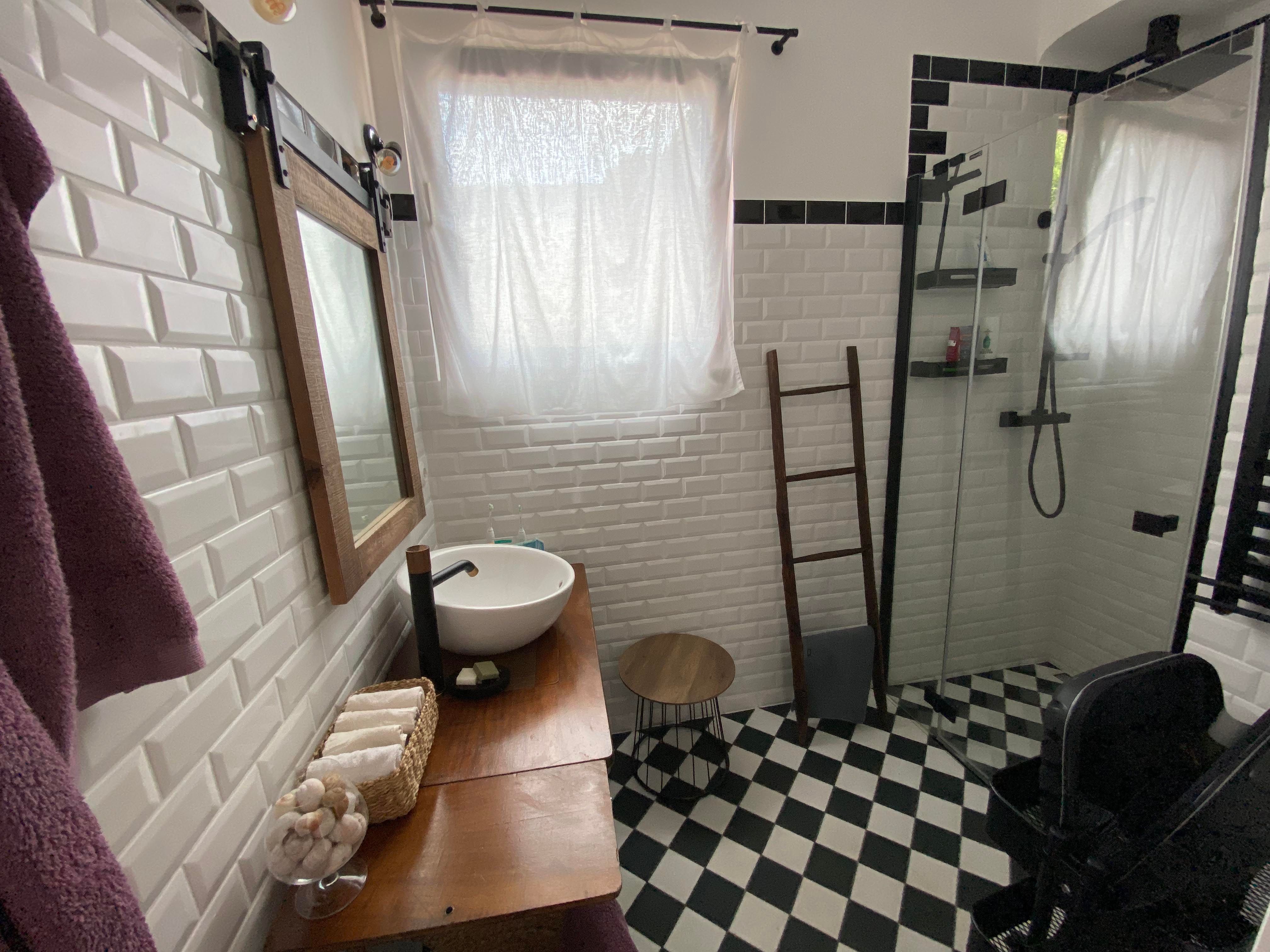 Modern bathroom with white tiled walls, black and white checkerboard floor, washbasin, mirror and shower.