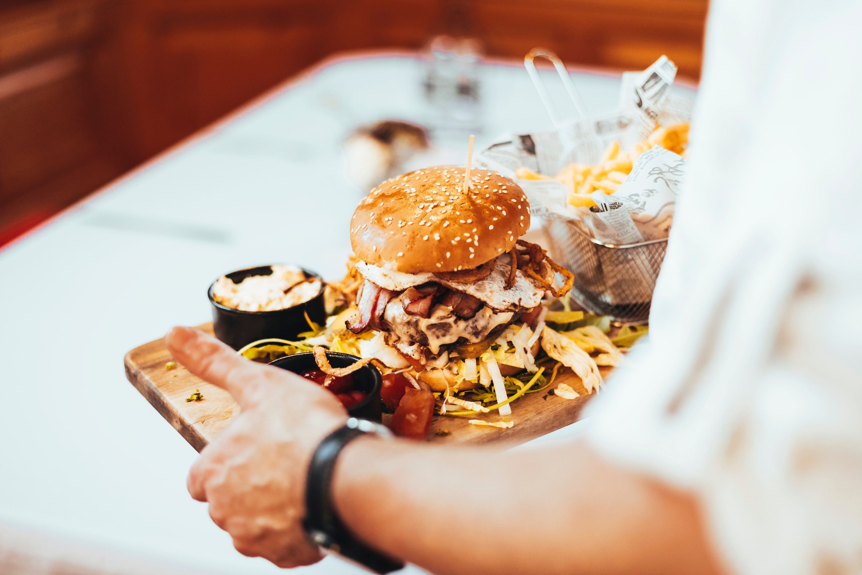 A burger with a sesame bun, bacon and fried egg on a wooden board, served with chips and dips.