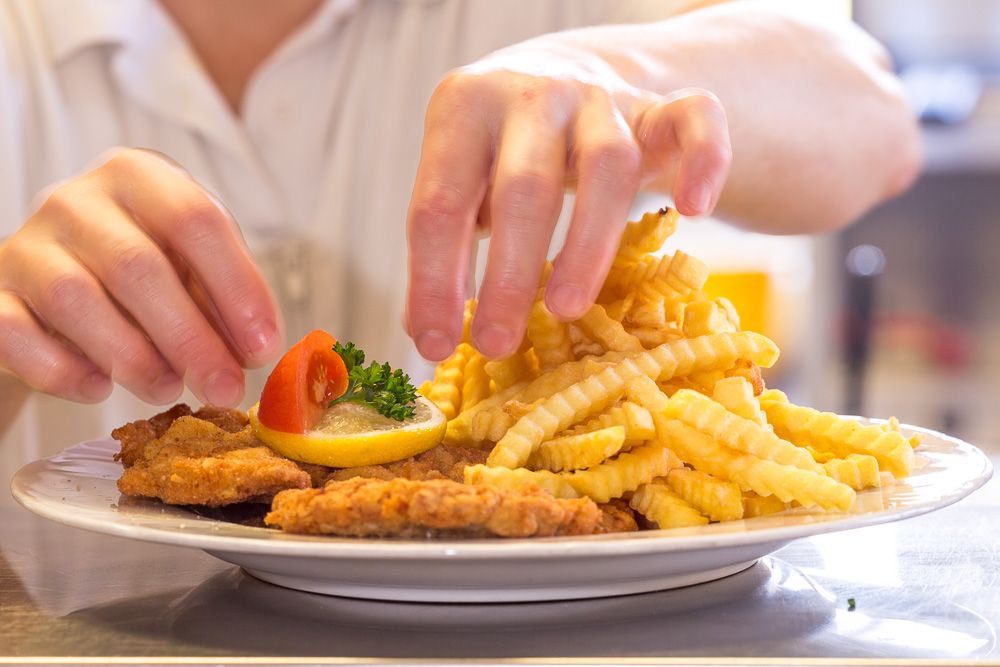 A plate with Wiener Schnitzel, French fries, lemon and tomato is served by one person.