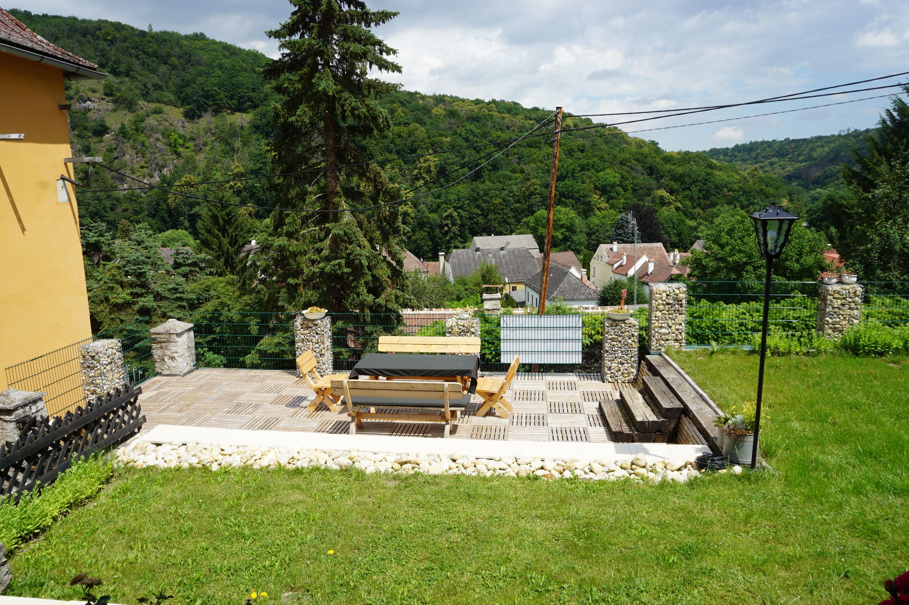 Terrace with wooden furniture and views of a village and wooded hills.