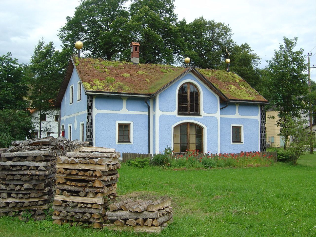 Blue house with grass roof and piles of wood in the foreground.