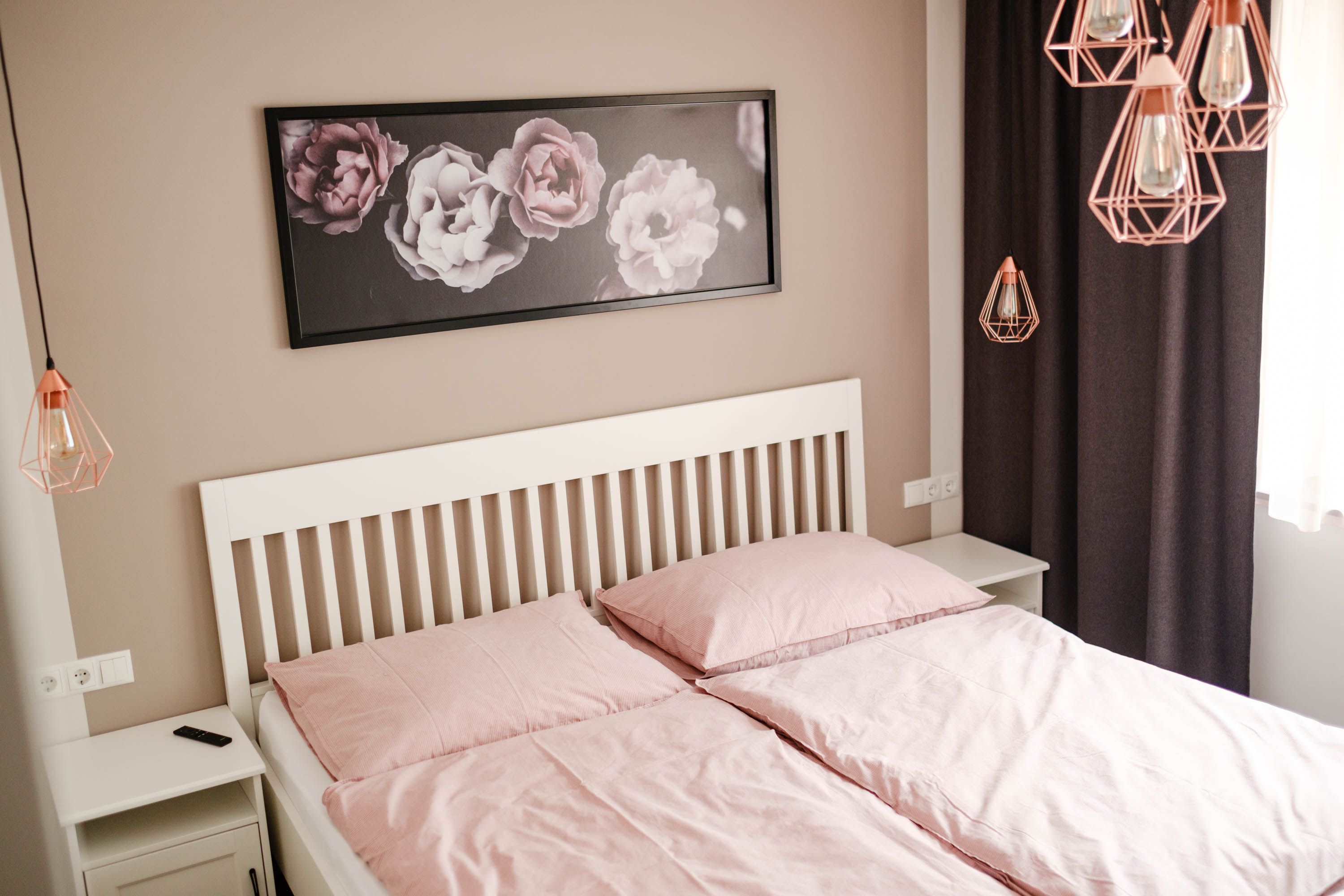 Bedroom with pink bed linen, white bed frame and flower picture on the wall.