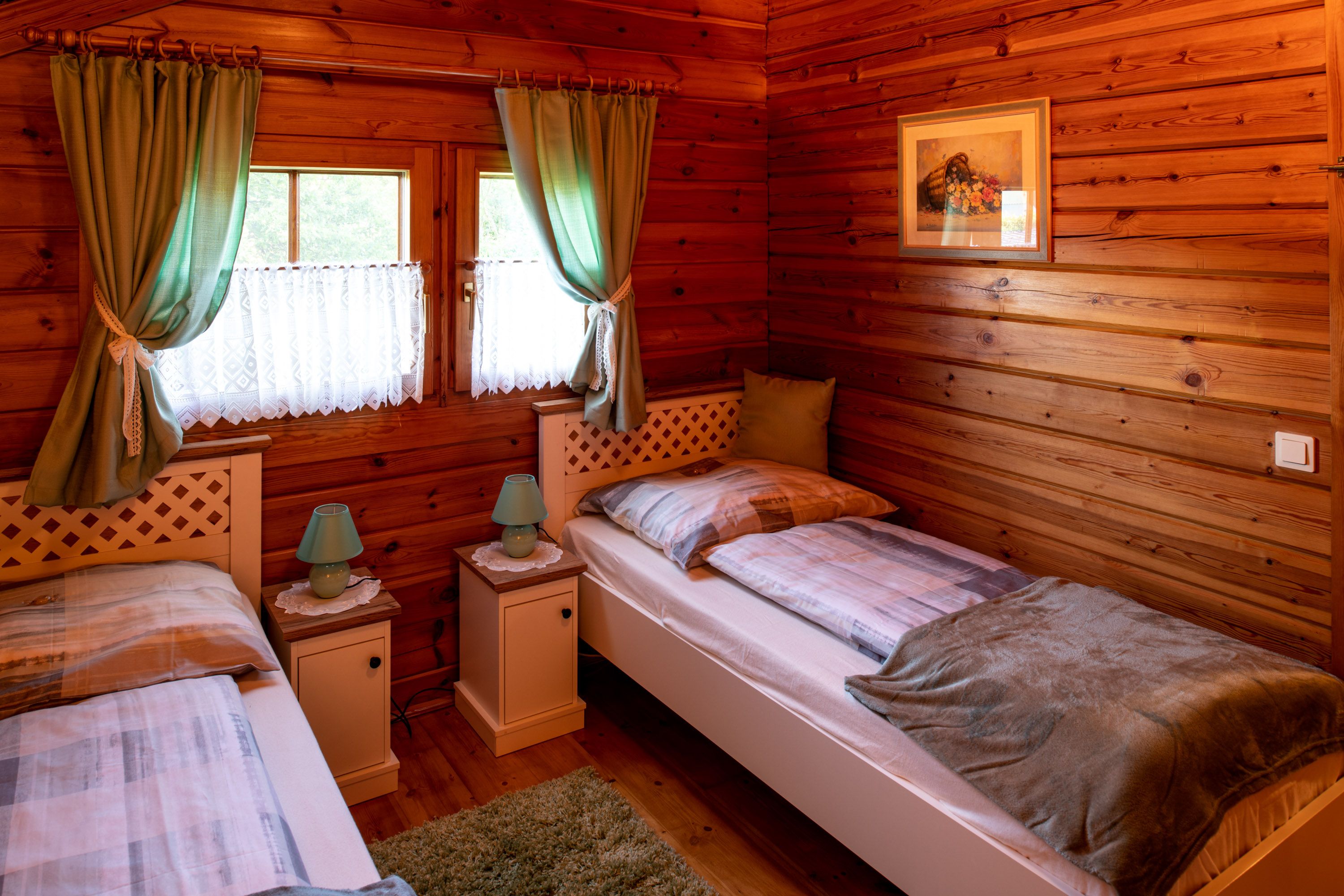 Cozy bedroom with wooden walls, two single beds, green curtains and bedside tables with lamps.