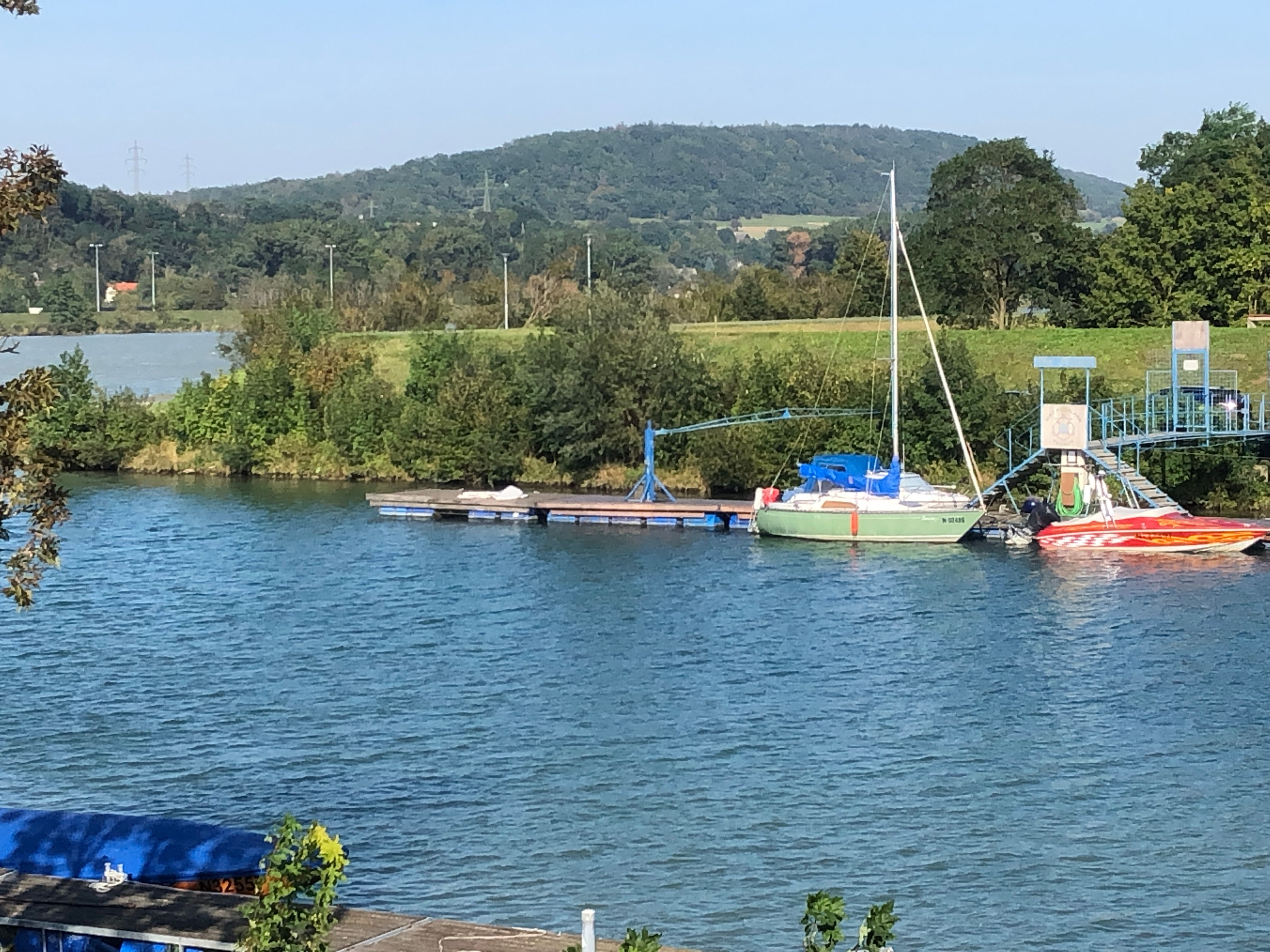 Boats on a jetty on a river with wooded hills in the background.