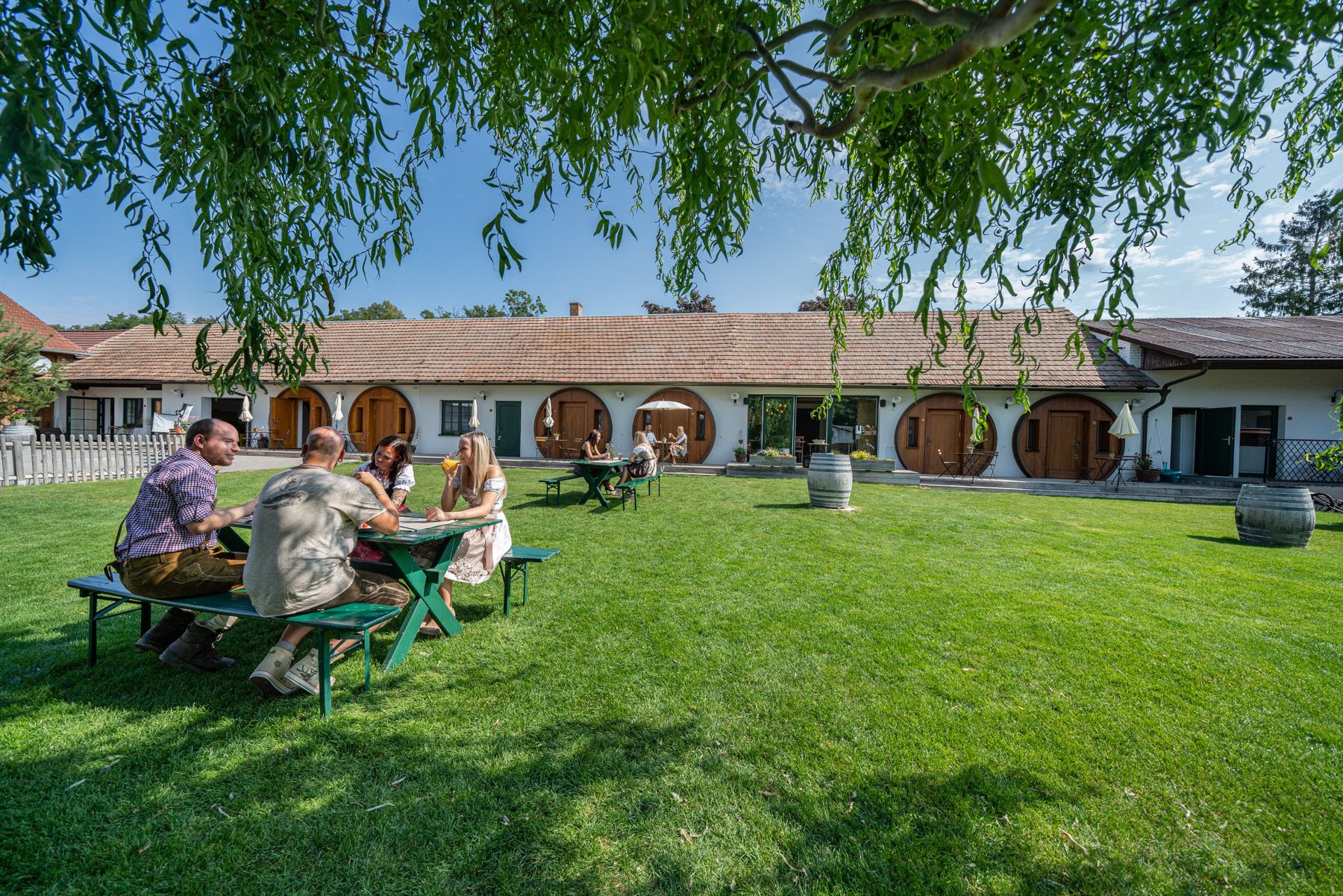 People are sitting at a table on a lawn in front of a building with round doors.