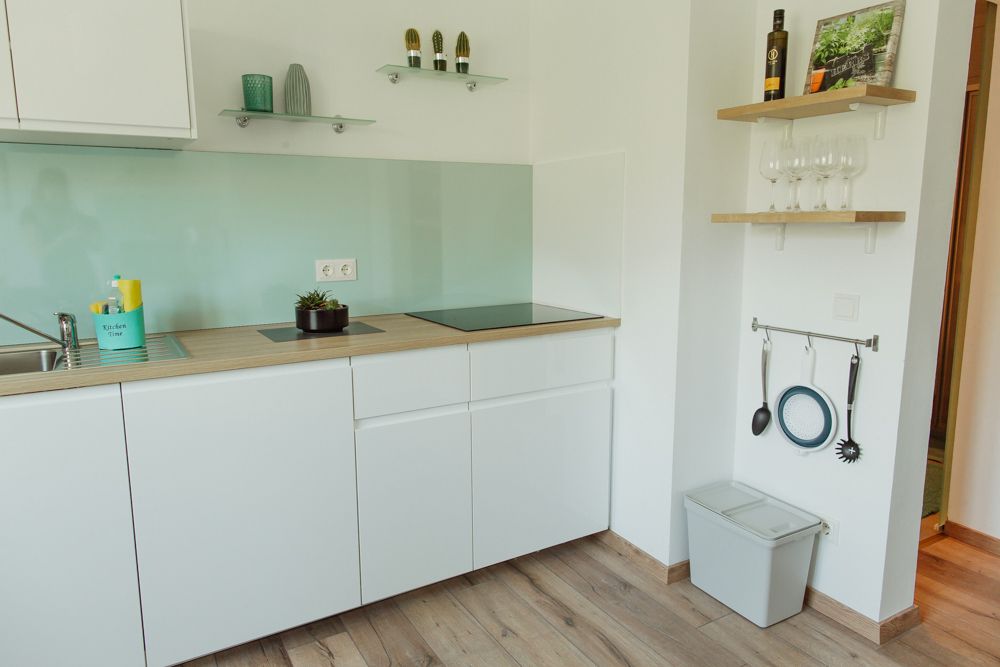 Modern kitchen with white cupboards, glass splashback and wooden shelves.