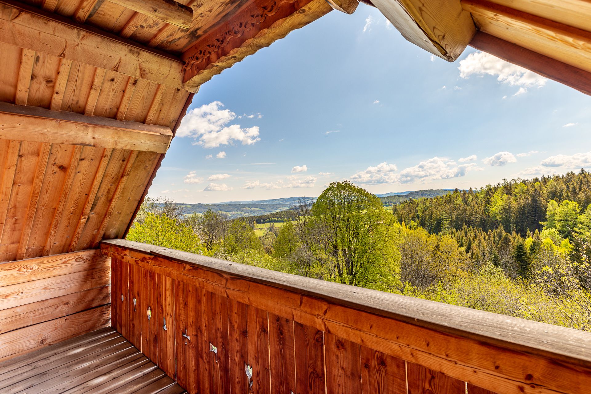 View from wooden balcony of green landscape with hills, trees and blue sky.