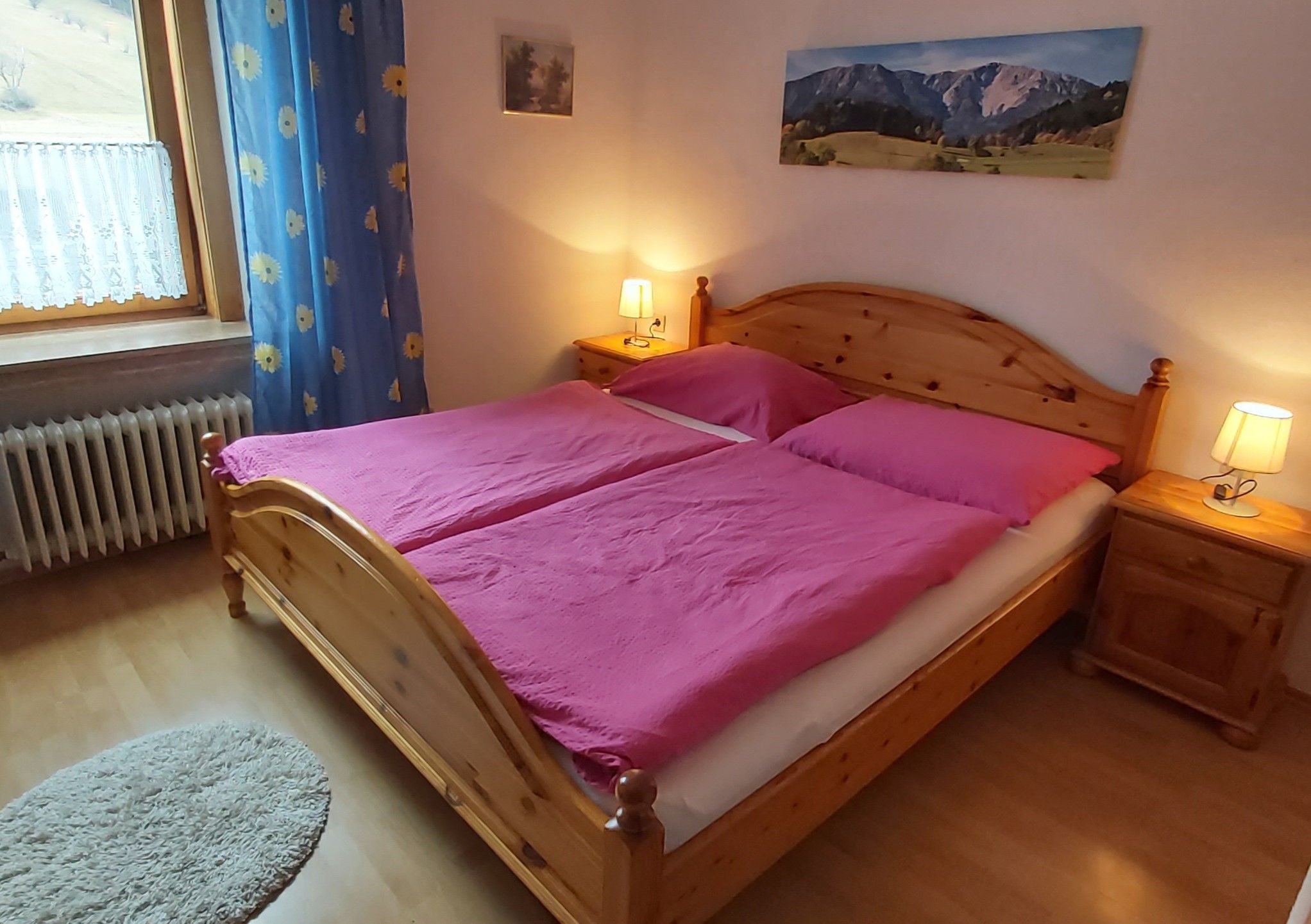 Cozy double room with wooden bed, pink bed linen and bedside tables with lamps.