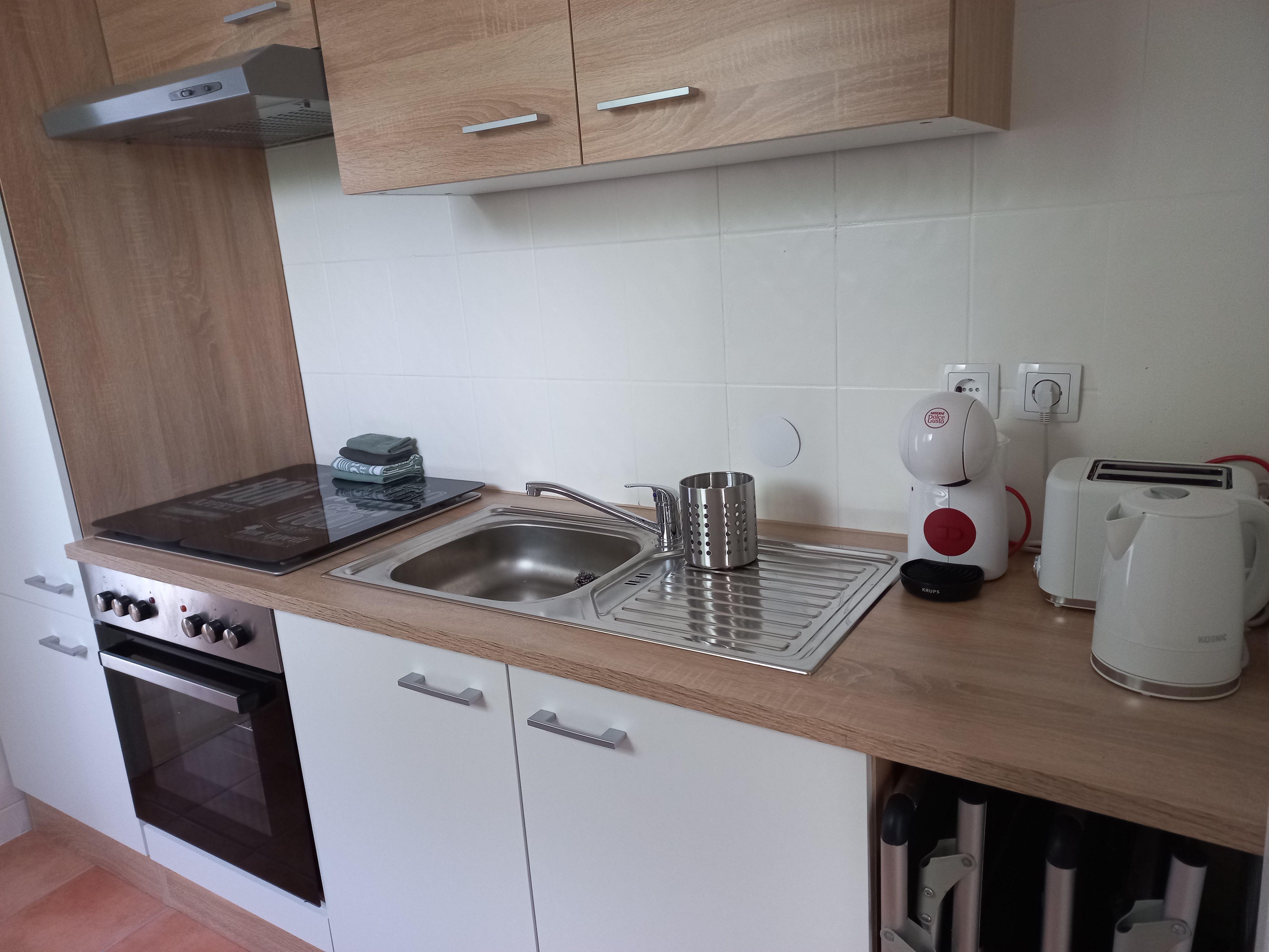 Modern kitchenette with stove, sink, coffee machine, toaster and kettle.