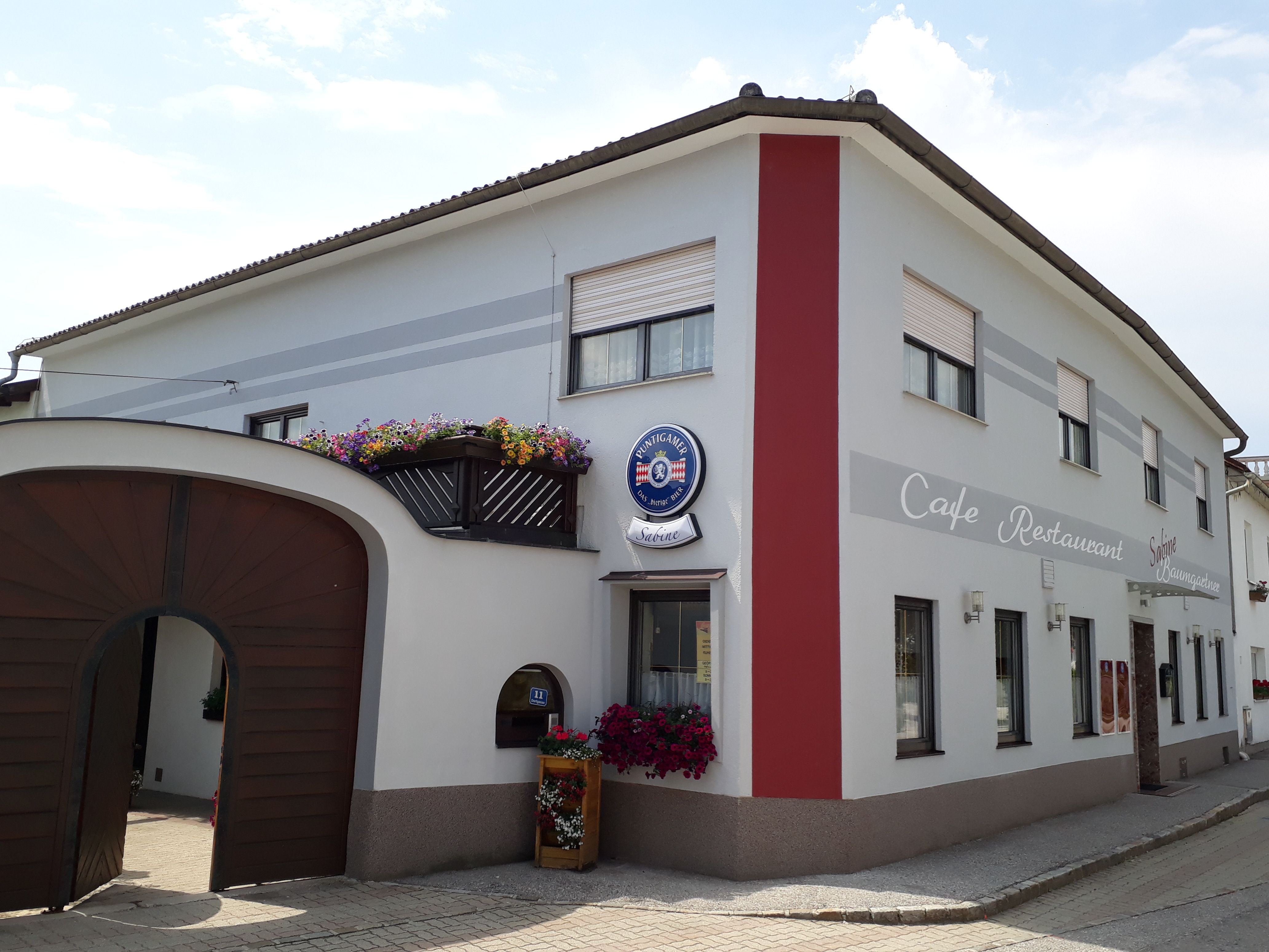 Exterior view of Café Sabine with wooden gate, white and red façade and the inscription "Café-Restaurant".