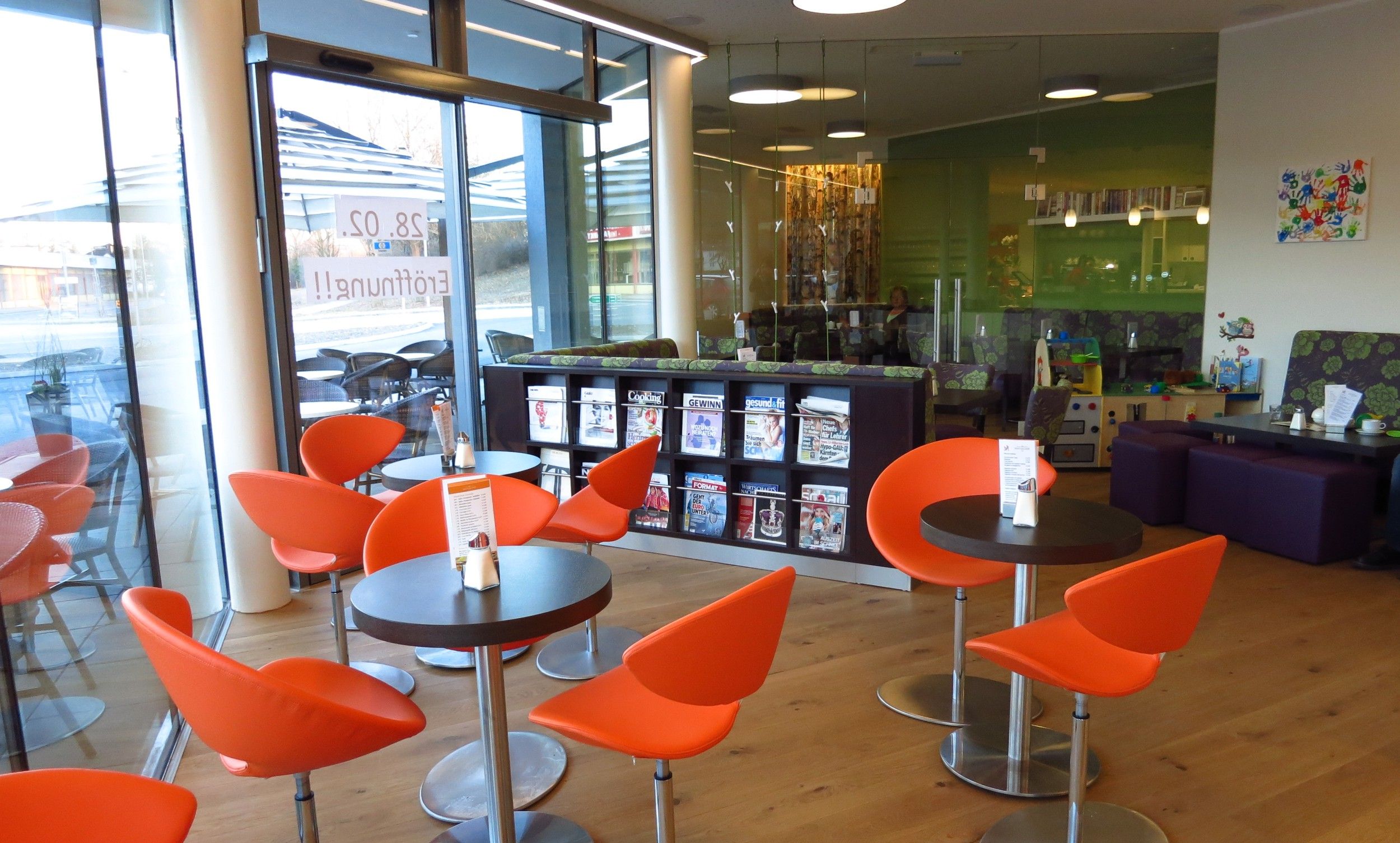 Interior view of a modern café with orange chairs and magazine rack.
