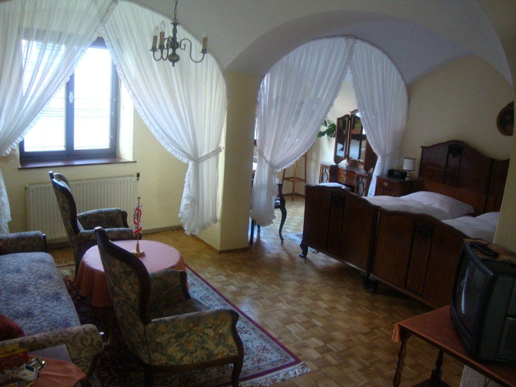 A cozy guest room with antique furniture, a double bed, armchairs and a small TV. Curtains separate the sleeping area.