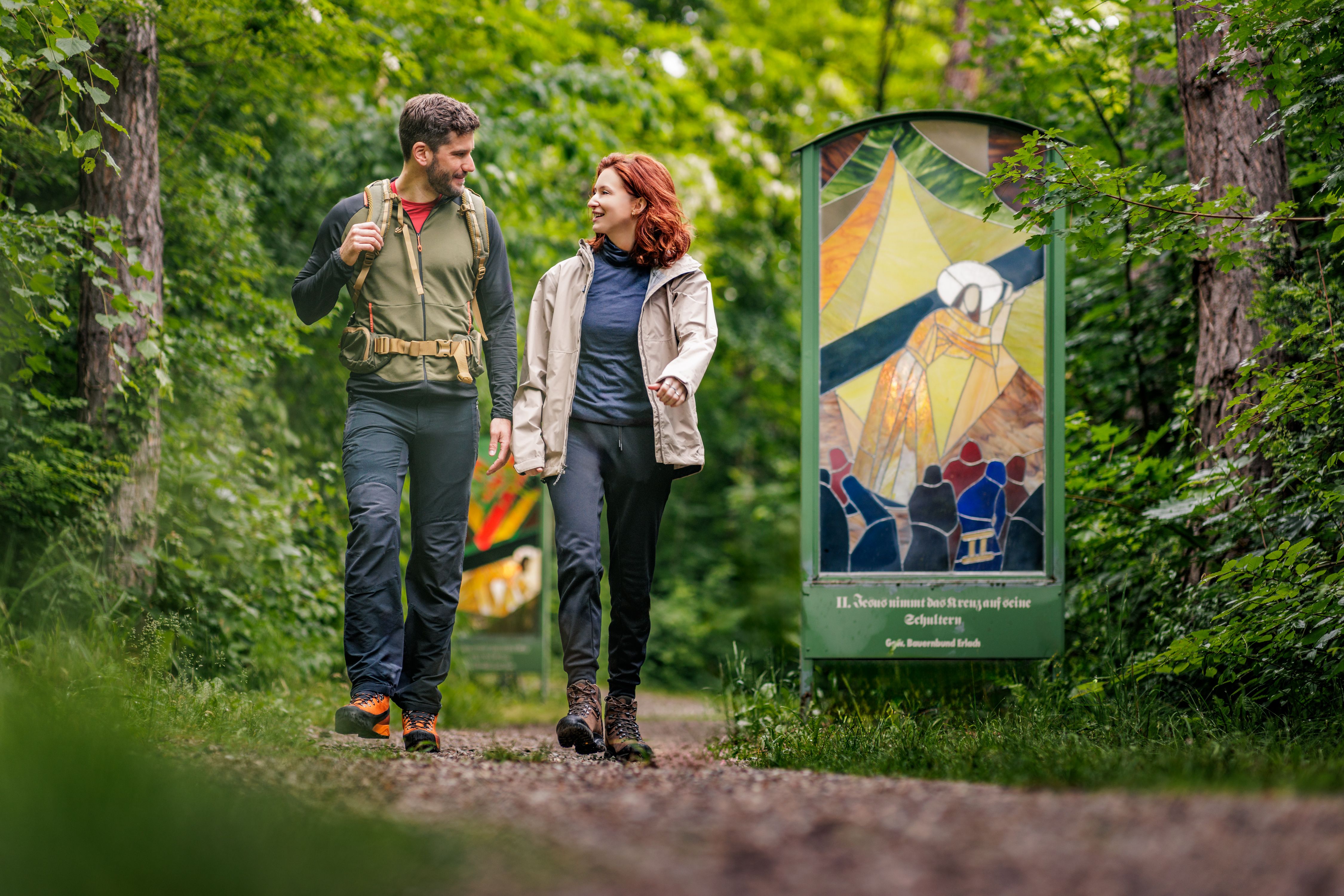 A couple walks along a forest path next to a colorful glass installation.