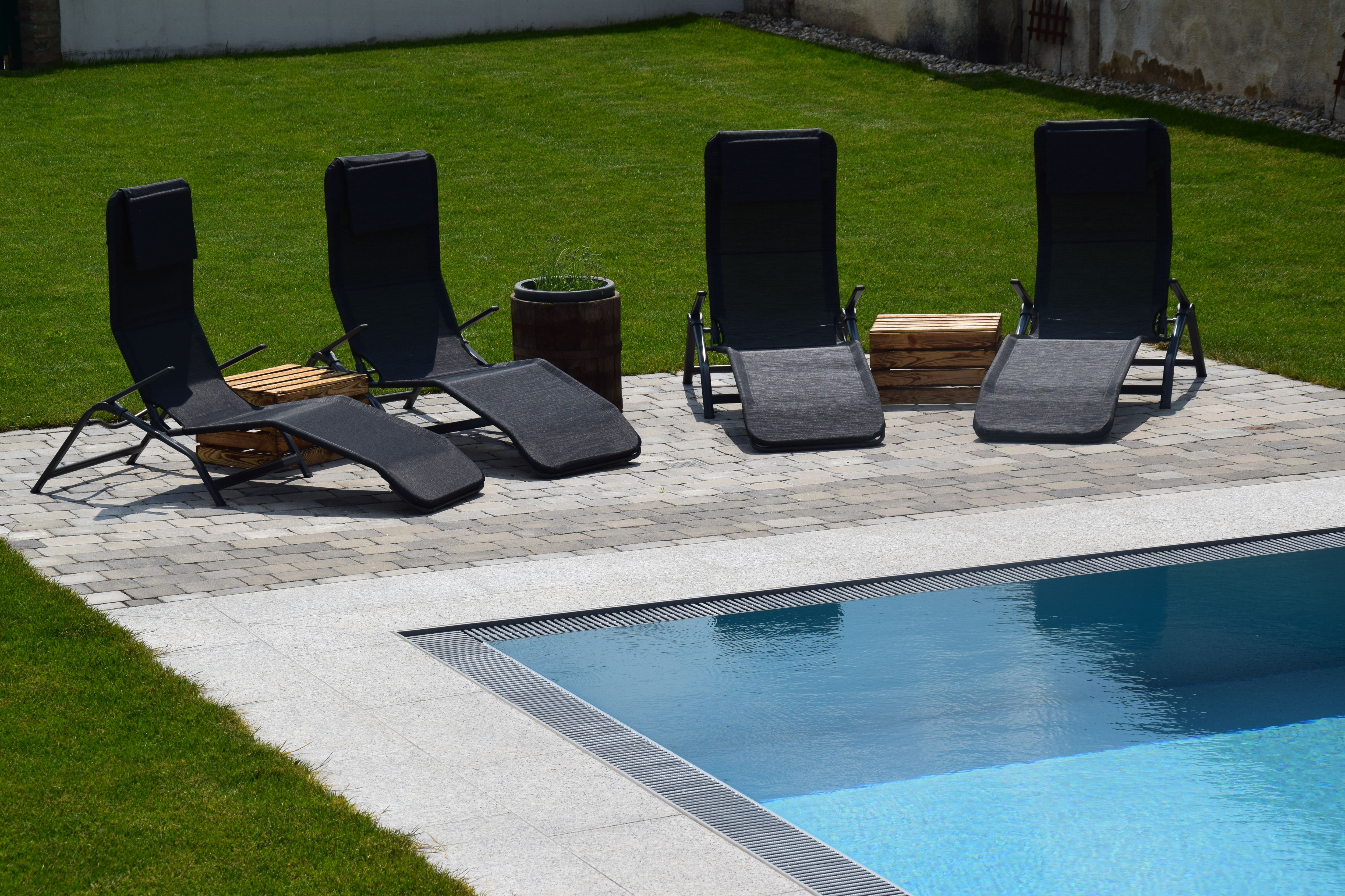 Four black sun loungers by the pool on a paved area in the garden.