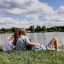 Three people sit on a meadow by the lake and look out over the water.