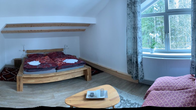 Cozy bedroom with wooden bed, sofa and large window with curtains.