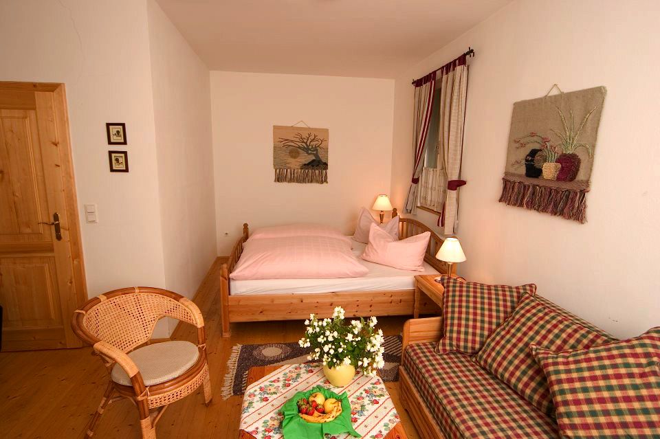 Cozy guest room with wooden furniture, a bed, a sofa, a table with flowers and fruit, and wall decorations.