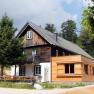 A traditional wooden house with extension in a rural setting, surrounded by trees and meadows.