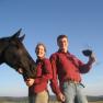 Two people in red shirts with a black horse and a large wine glass outside.