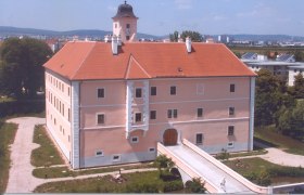 Vösendorf Castle with red roof and clock tower, surrounded by green spaces.