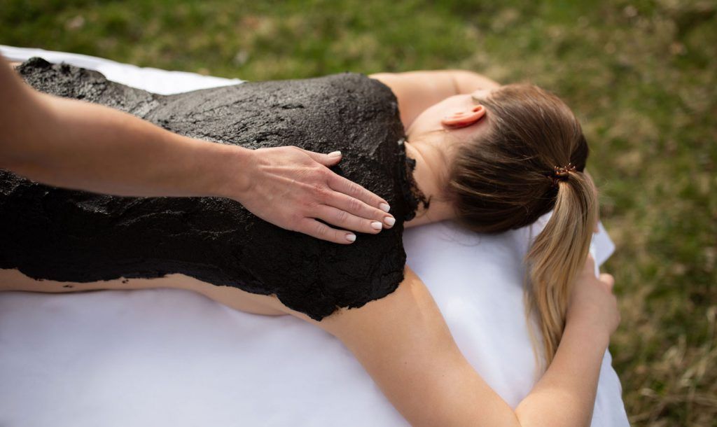 person receives a mud pack on their back in the open air.