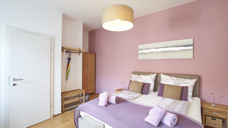 A cozy guest room with a pink wall, double bed and modern furnishings.