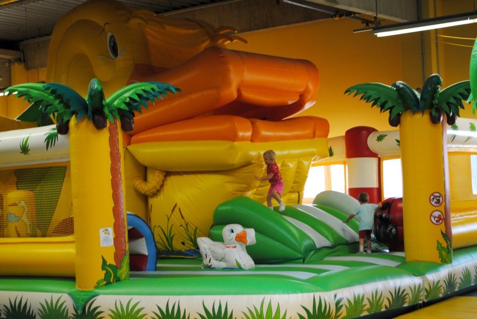 Inflatable bouncy castle with giant duck and palm trees, children play on it.