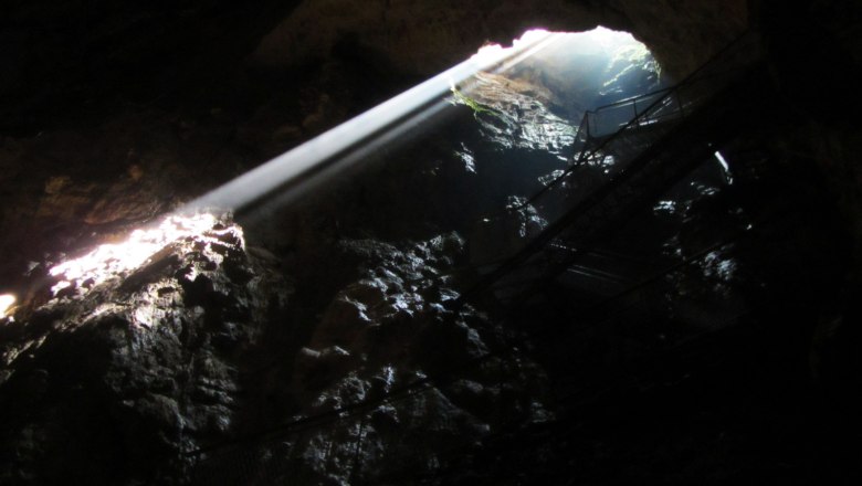 Rays of sunlight penetrate through an opening in a dark stalactite cave.