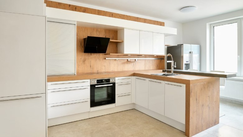 Modern kitchen with wood and white tones, stove, sink and large window.