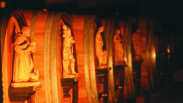Row of wooden barrels with carved figures in a wine cellar.