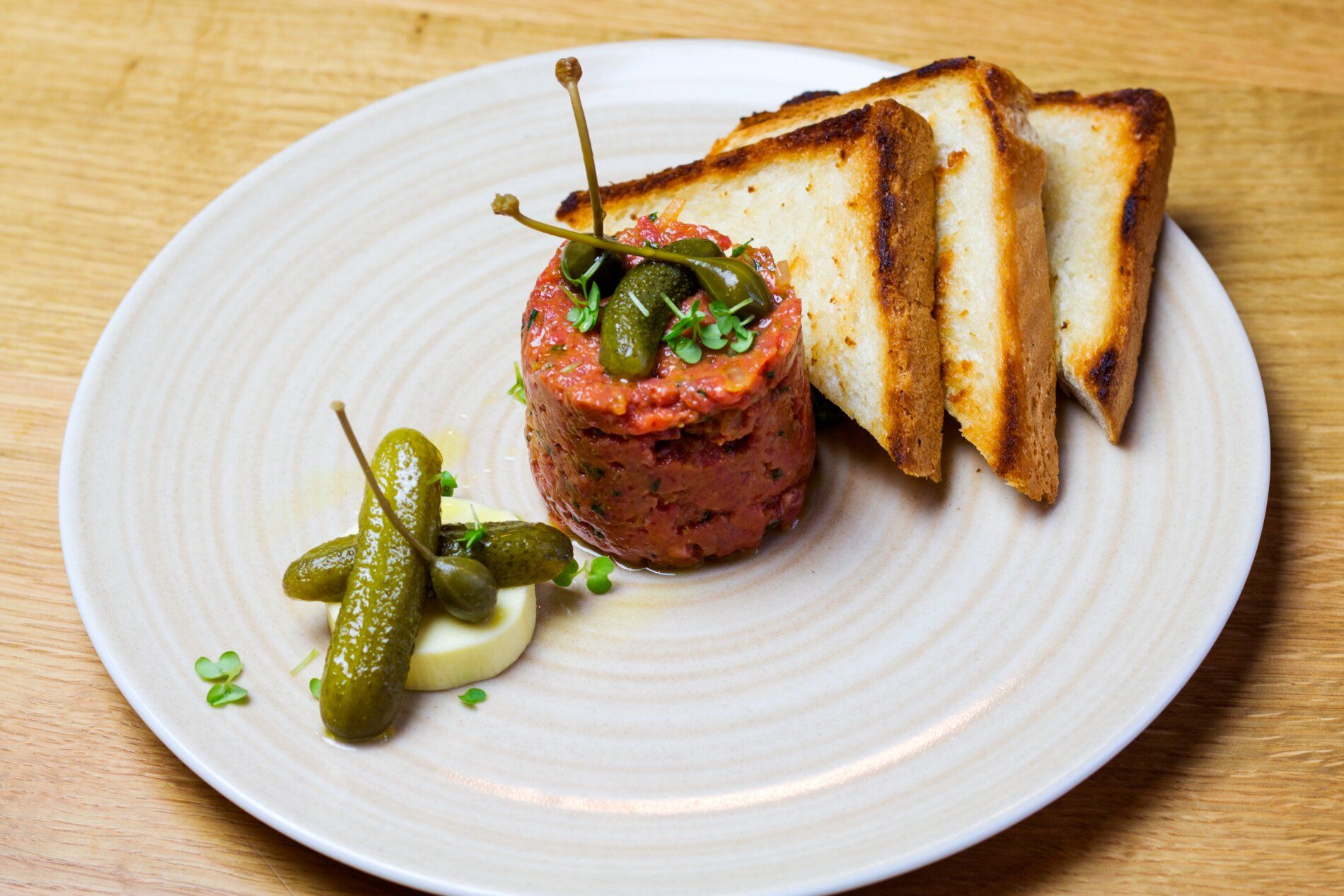 Beef tartare with capers, gherkins and toast on a plate.