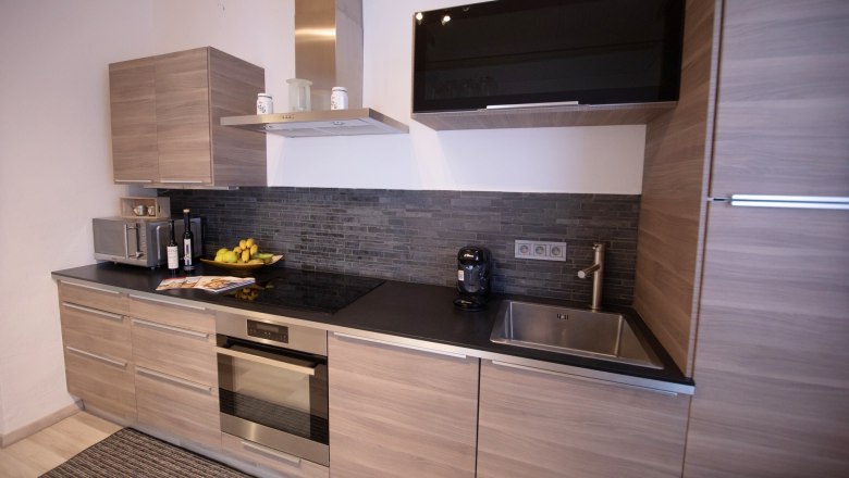 Modern kitchen with wooden cupboards, black worktop, sink, stove and extractor hood.