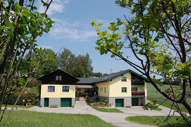 A large yellow vacation home with green garage doors, surrounded by trees and meadows.