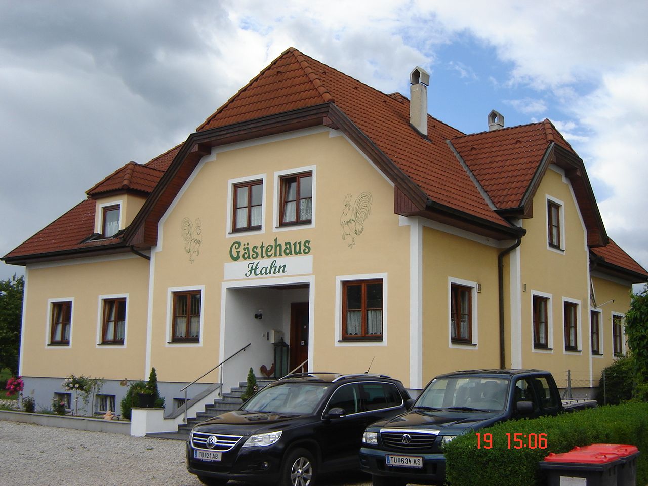 Yellow guest house with a red roof and parked cars in front of it.