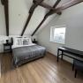 Modern bedroom with wooden beamed ceiling, double bed, wooden floor and window.