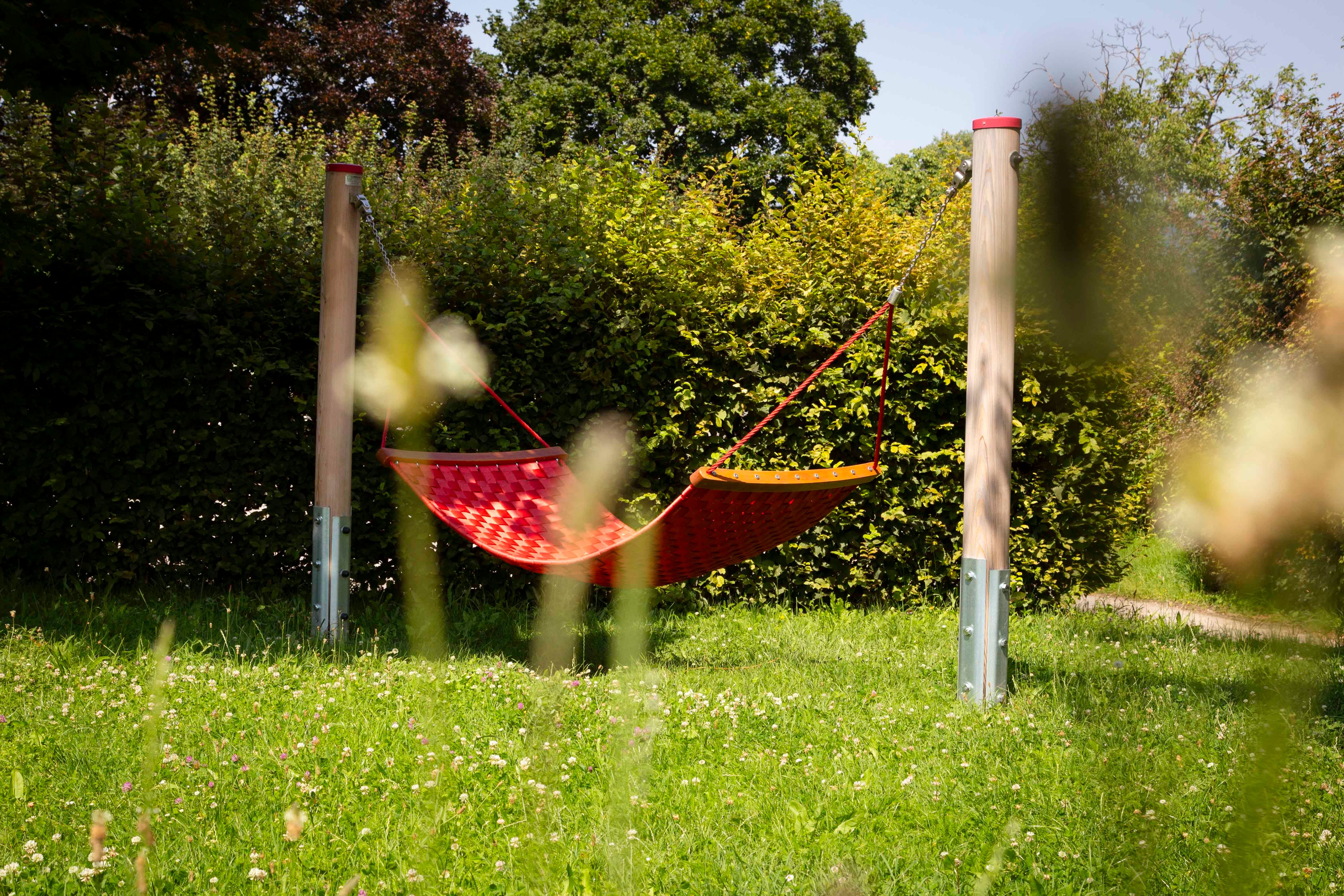 Red hammock on a playground surrounded by green vegetation.