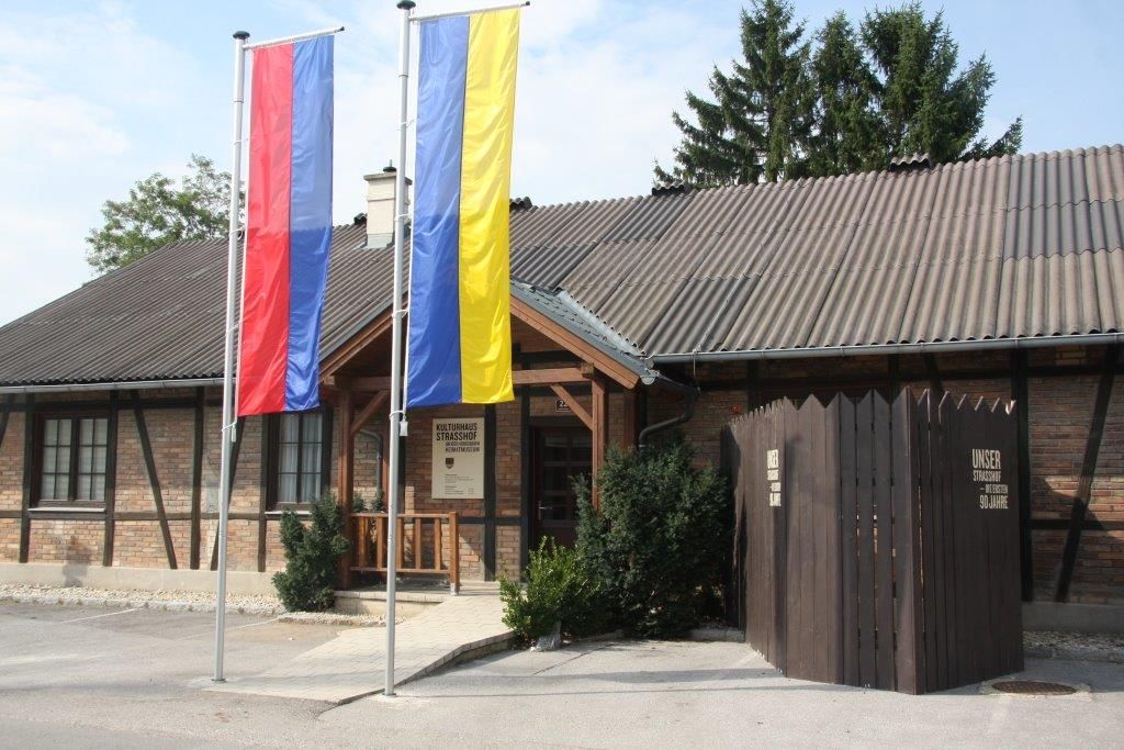 Entrance to the Strasshof museum of local history with two flagpoles and a wooden fence.