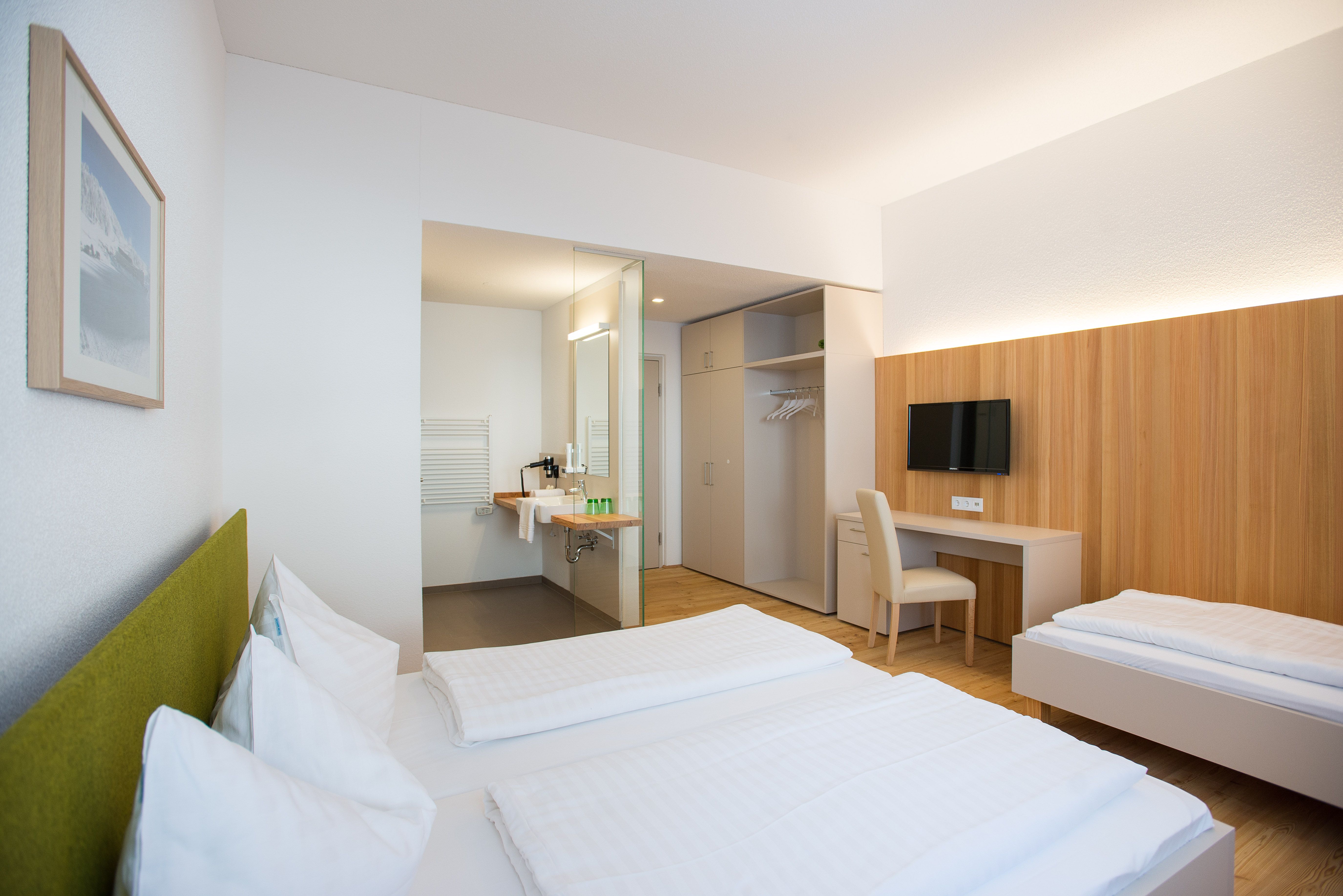 Modern furnished hotel room with two beds, desk, TV and open bathroom.