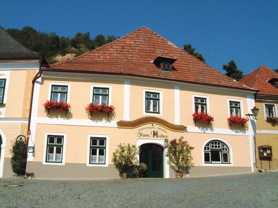 Exterior view of a traditional building with a yellow façade and red flowers on the windows.